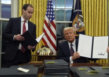 President Donald Trump holds up an executive order commuting sentences for people convicted of Jan. 6 offenses in the Oval Office of the White House, Monday, Jan. 20, 2025, in Washington. (AP Photo/Evan Vucci)