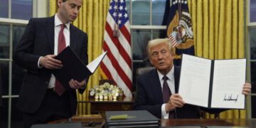 President Donald Trump holds up an executive order commuting sentences for people convicted of Jan. 6 offenses in the Oval Office of the White House, Monday, Jan. 20, 2025, in Washington. (AP Photo/Evan Vucci)